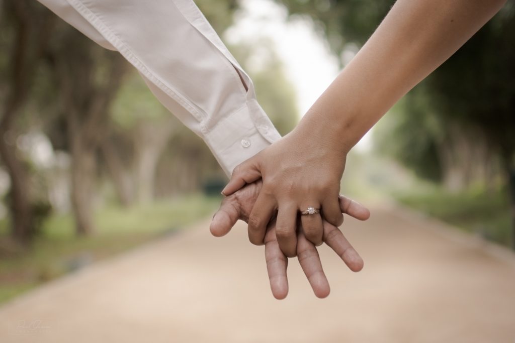 paul-garcia-gc0BvNeGfuM-unsplash | Elope to Australia Man and woman holding hands, engagement ring, pathway with green leaf trees