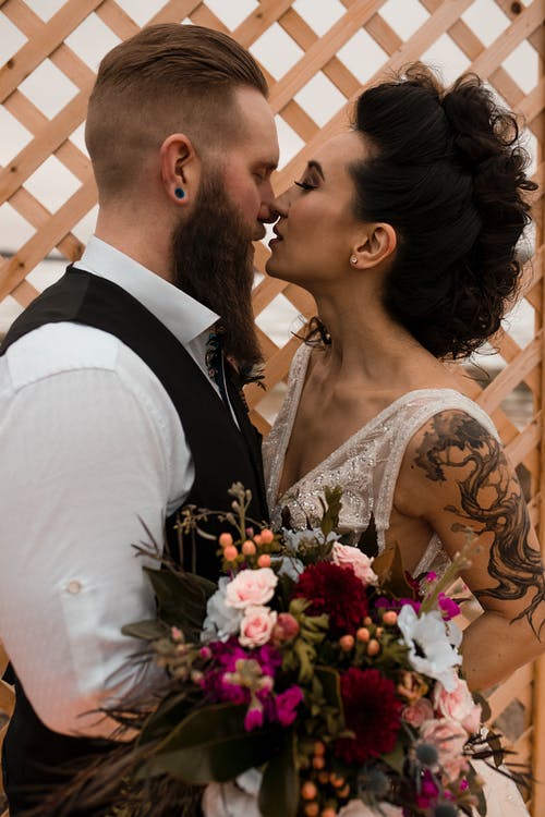 pexels-photo-2496336 | Elope to Australia groom with beard kissing bride with sleeve tattoo holding bouquet